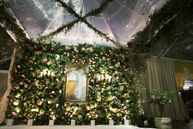 Wall of greenery and pink flowers at wedding reception