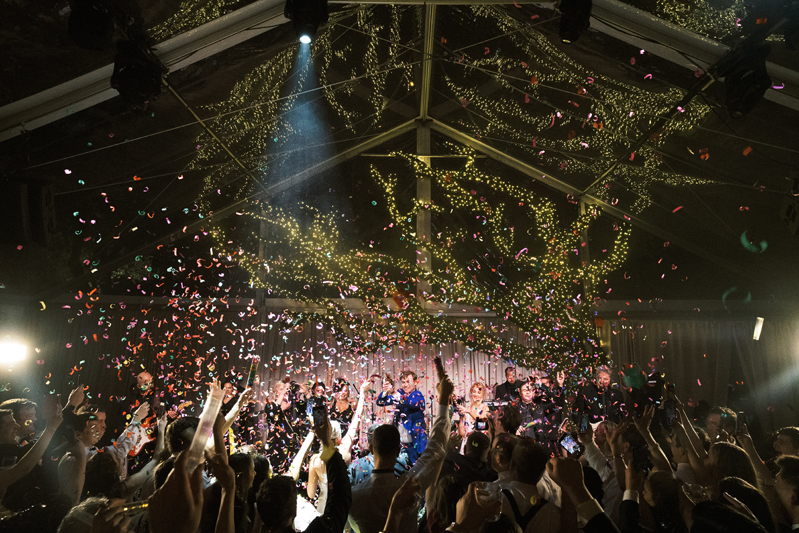 Tented wedding reception with crowded dance floor and confetti cannons.