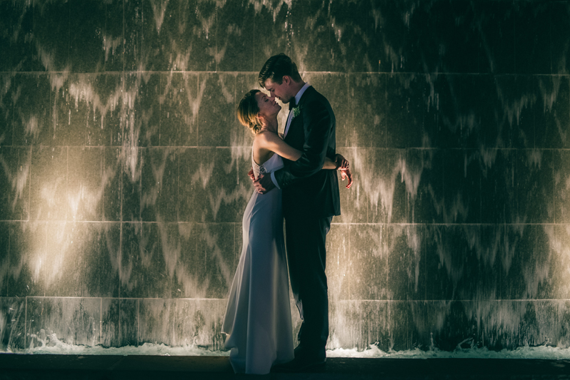 bride and groom in front of city waterfall