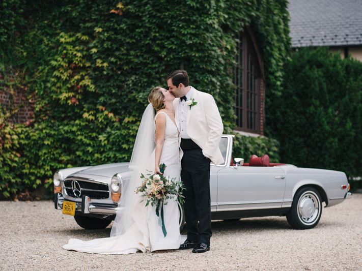 Bride and groom kissing in front of vintage car