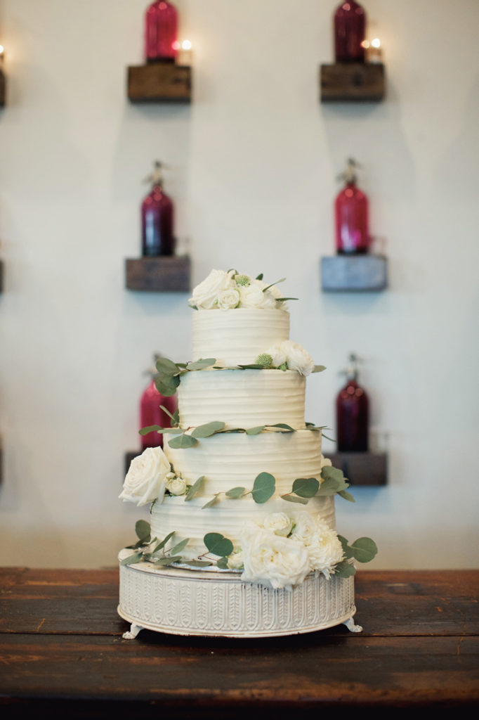 Four tier wedding cake with white flowers and greenery.